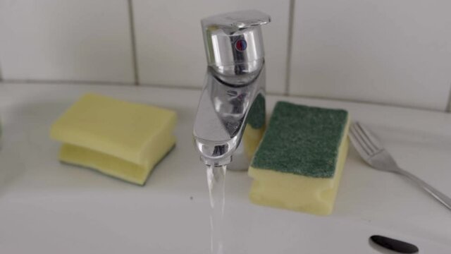 Water tap on a sink with two sponges on it being turnt on