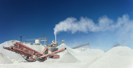 Panorama of industrial stone crushing equipment on the background of hills of crushed stone and blue sky.