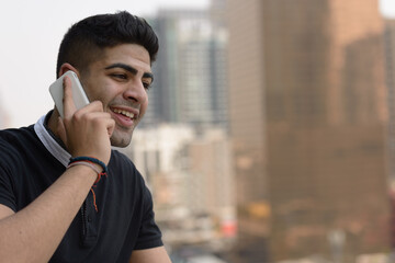 Face of happy young handsome Indian man talking on the phone in the city