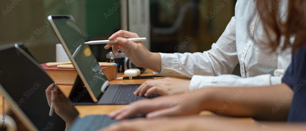 Poster two female workers consulting on their project while working with mock-up tablet on wooden table