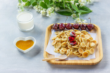Tiny  pancakes cereal, cherries, milk and honey. Decorated with sprigs of Jasmine on a light background. Trendy  food, home breakfast. Funny food for kids.