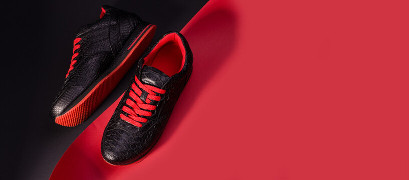 Fashionable snakeskin leather sneakers. Black sneakers with bright red bootlaces against a black and red background.