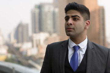 Face of young handsome Indian businessman thinking in the city