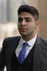 Face of young handsome Indian businessman thinking in the city