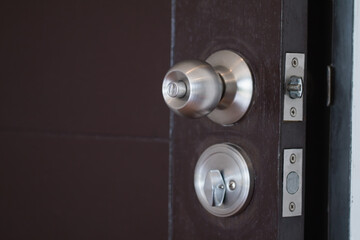 Closeup stainless steel knob, brown wooden door lock. The image is partially clear.