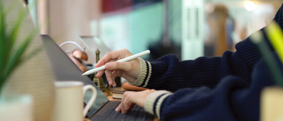 Female hands using digital tablet with stylus pen on office desk with decoration and coffee cup