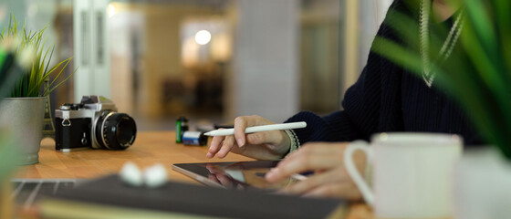 Female photographer working on digital tablet with stylus pen on wooden table with camera and decorations