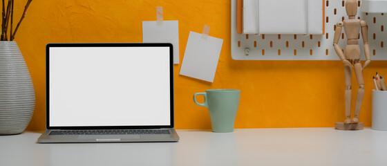 Blank screen laptop on creative home office desk with mug, stationery and decorations