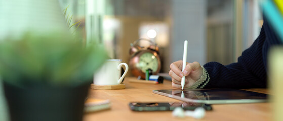 Female hands using digital tablet with stylus on wooden home office desk with smartphone, supplies and decorations