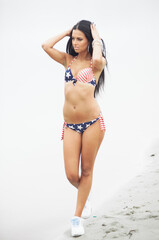 A woman in a swimsuit with an American flag walks along the coast