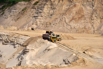 Wheel front-end loader loading sand into heavy dump truck at the opencast mining quarry. Dump truck transports sand in open pit mine. Quarry in which sand and gravel is excavated from the ground.