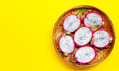 Ripe dragonfruit or pitahaya in wooden bamboo threshing basket on yellow background.