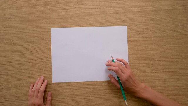 Top view of crop anonymous female artist sitting at wooden desk with pointed pencil with eraser on top and sheet of empty paper
