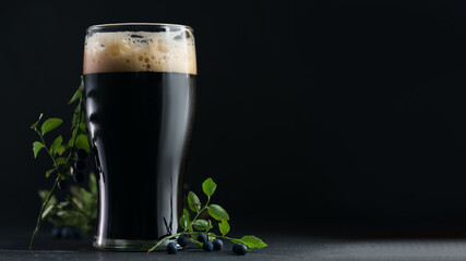 Blueberry craft beer stout in a glass on a dark background with berries copy space