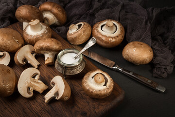 Fresh champignon mushrooms on a cutting board and on a black background