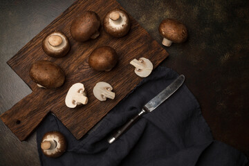 Fototapeta na wymiar Fresh champignon mushrooms on a cutting board and on a black background