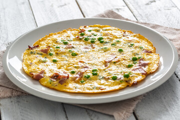Omelette with prosciutto peas and herbs on white plate
