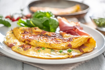 Omelette with prosciutto peas basil tomatoes and herbs on white plate