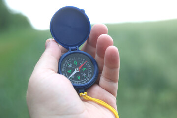 Old classic navigation compass in hand on natural background as symbol of tourism with compass,...