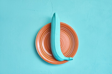 painted banana turquoise color on an orange ceramic plate. creativity design concept