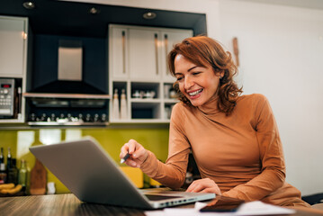 Happy woman using laptop in the kitchen, portrait.