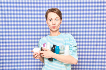 Surprised girl with problem face skin is holding many cosmetic bottles