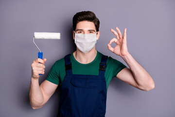 Close-up portrait of his he attractive healthy guy painter wearing safety cotton mask mers cov influenza infection prevention drawing wall building showing ok-sign isolated grey color background