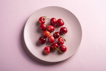 Fresh ripe cherry fruits on pink plate, summer vitamin berries on minimal background, angle view