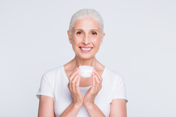 Portrait of lovely grandmother holding jar with nourishing procedure looking at camera wearing...