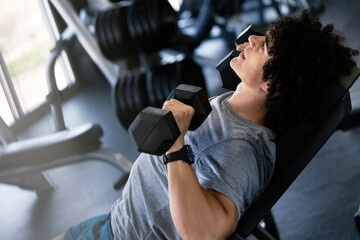 Muscular man working out in gym doing exercises with dumbbells at biceps - obrazy, fototapety, plakaty