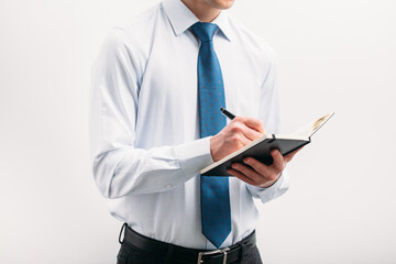 The guy writes in a black notebook. A man on a white background with a blue tie in a white shirt. Note in the notebook..