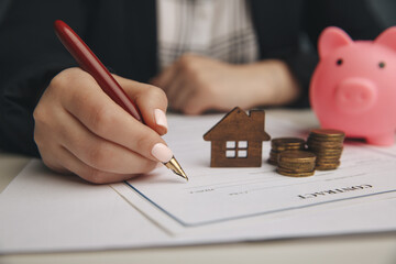 Close up wooden toy house with Woman signs a purchase contract or mortgage for a home, Real estate...