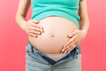 Close up of naked pregnant woman's belly wearing opened jeans at colorful background with copy space. Pregnancy concept