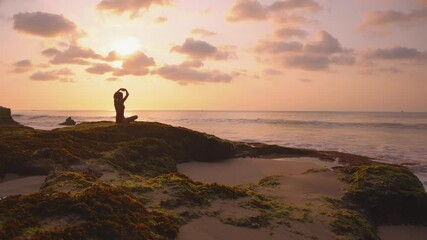 Solo activity and self isolation. Young woman silhouette doing stretching exercise and meditating with beautiful view of sea and sunset. Harmony and spirituality concept. Yoga and healthy lifestyle.