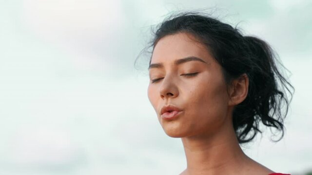 Brunette portrait doing breathing exercises while the wind waving hair. Asian young woman doing yoga and stretching on the hill. balance and harmony with nature. Concept of welless, yoga poses.