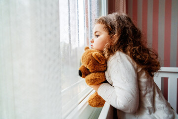 Little cute girl is watching from window to the rain with sadness get bored. 
