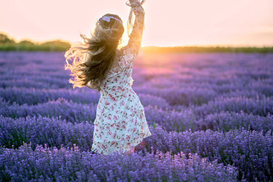 Happy woman dancing in a lavender field at sunset. Beautiful flowers meadow. Summer sunset colorful lighting