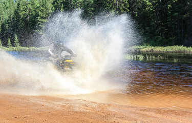 Man driving motocross ATV quad through splashing river lake water with high speed. Foy, Foyross Lake, Sudbury, Canada.