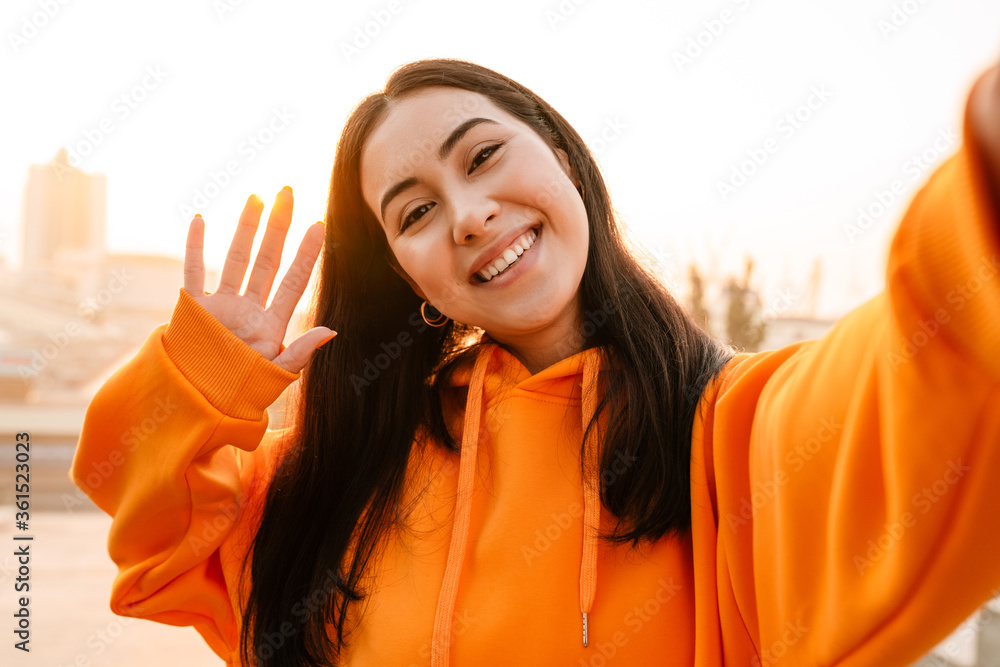 Sticker photo of asian woman smiling and waving hand while taking selfie photo