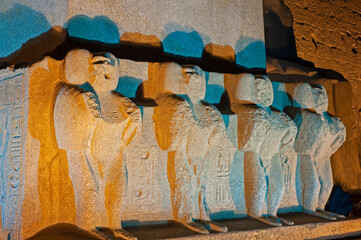 Statues at base of obelisk by entrance to Luxor Temple during night