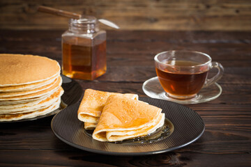 puncakes with honey and cup of tea on old wooden background