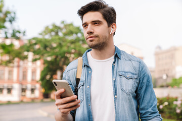 Photo of focused man with earphone using cellphone while walking