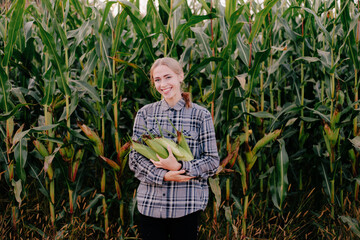 Beuatiful positive blonde girl in corn field with maze in hands farm rural girl shows corn maize in her hand on blurred background, Sweet white smile