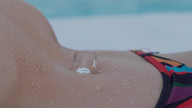 Ice cube on the girl&rsquo;s stomach. Beautiful girl's stomach in drops of water on a background of the pool.