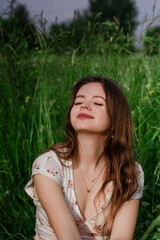 Soft focus close up of Young brunette girl in white top and sitting in green meadow field grass in countryside looking a side touching her hair and enjoy nature and rural life Solo out door activity