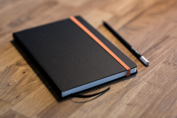 Black business notebook and regular pencil on a vintage wooden desk.