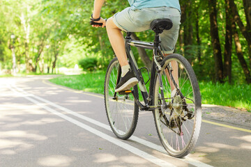 Fototapeta na wymiar Man in blue t-shirt and blue jeans shorts cycling in the nature on bicycle on outdoor trail in park. Active summer solo outdoor activity. Concept of training, sport activity and health care.