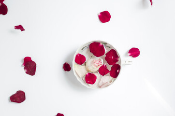 High angle view of cup with bright red rose petals and white pink rose bud floating in a cup on white background