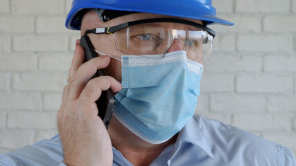 Engineer with Safety Helmet and a Protection Mask on His Face Talking to the Cell Phone