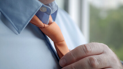Elegant Businessman Image Wearing Blue Shirt and Making a Knot to an Orange Tie.